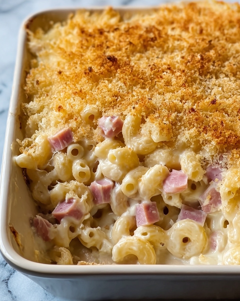 The image shows a close-up of a baked macaroni and cheese dish in a white square baking dish. It has three main layers: the bottom layer is creamy, white pasta mixed with creamy cheese sauce and small cubes of pink ham scattered throughout. The top layer is a golden-brown, crunchy breadcrumb crust, evenly spread and toasted perfectly. The pasta is elbow-shaped, and the cheese sauce looks rich and smooth, holding the pasta and ham together. The dish is set against a white marbled texture background. Photo taken with an iphone --ar 4:5 --v 7