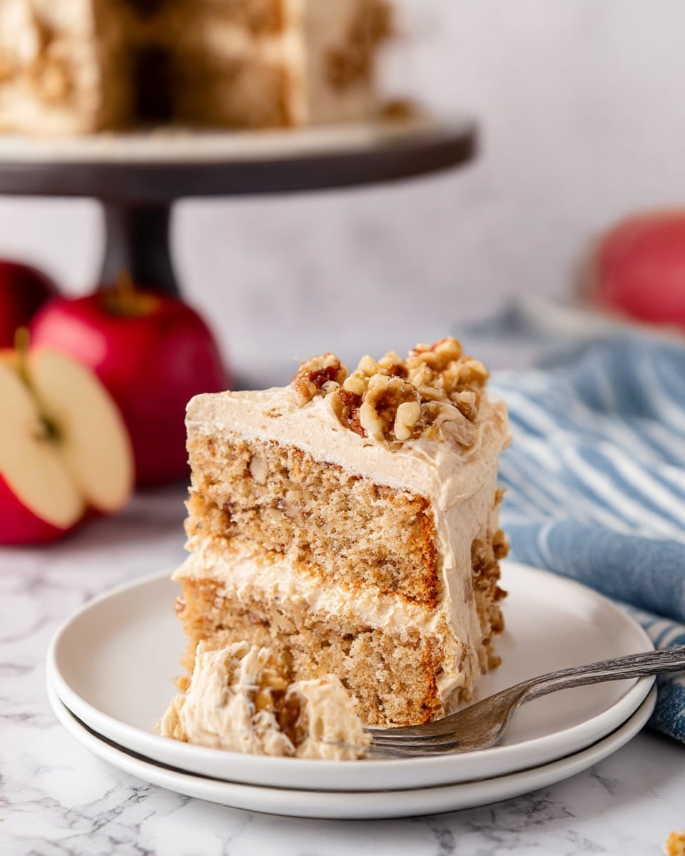 The image shows a slice of two-layered cake on a white plate. The cake layers are light brown with a crumbly texture and bits of walnut inside. Between the layers and on top, there is a thick, creamy beige frosting with a smooth and slightly whipped texture. The top layer of frosting is sprinkled with chopped walnuts. There is a piece of cake on a fork placed on the plate near the slice. The background includes a white marbled surface, a blue and white striped cloth, two red apples, and a blurred dark cake stand holding the rest of the cake. photo taken with an iphone --ar 4:5 --v 7
