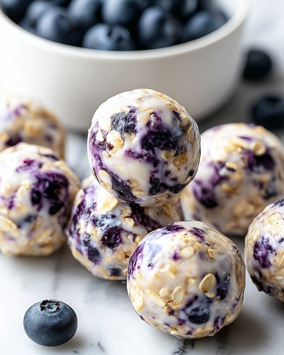 The image shows a close-up of several small round balls made from oats and blueberries, placed on a white marbled surface. Each ball has a creamy white base mixed with light brown oat pieces and has blueberry spots that add purple and dark blue colors throughout. The balls have a slightly glossy, smooth texture, showing the mixture is moist. In the background, there is a white bowl filled with fresh blueberries, slightly out of focus, and a few loose blueberries are scattered on the marble surface. photo taken with an iphone --ar 4:5 --v 7