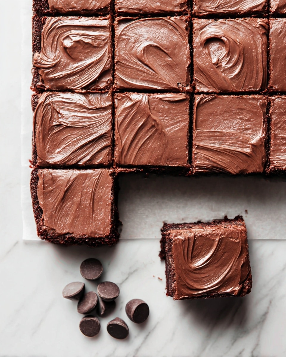 A tray of nine dark chocolate brownies is shown, each cut into even squares and topped with a smooth layer of thick, creamy chocolate frosting that has gentle swirls and waves. One brownie is slightly pulled away from the tray, showing its rich, moist interior beneath the frosting. Below the brownies, three dark chocolate chips rest on a white marbled surface. The overall texture contrasts between the soft brownies and the shiny, thick frosting photo taken with an iphone --ar 4:5 --v 7