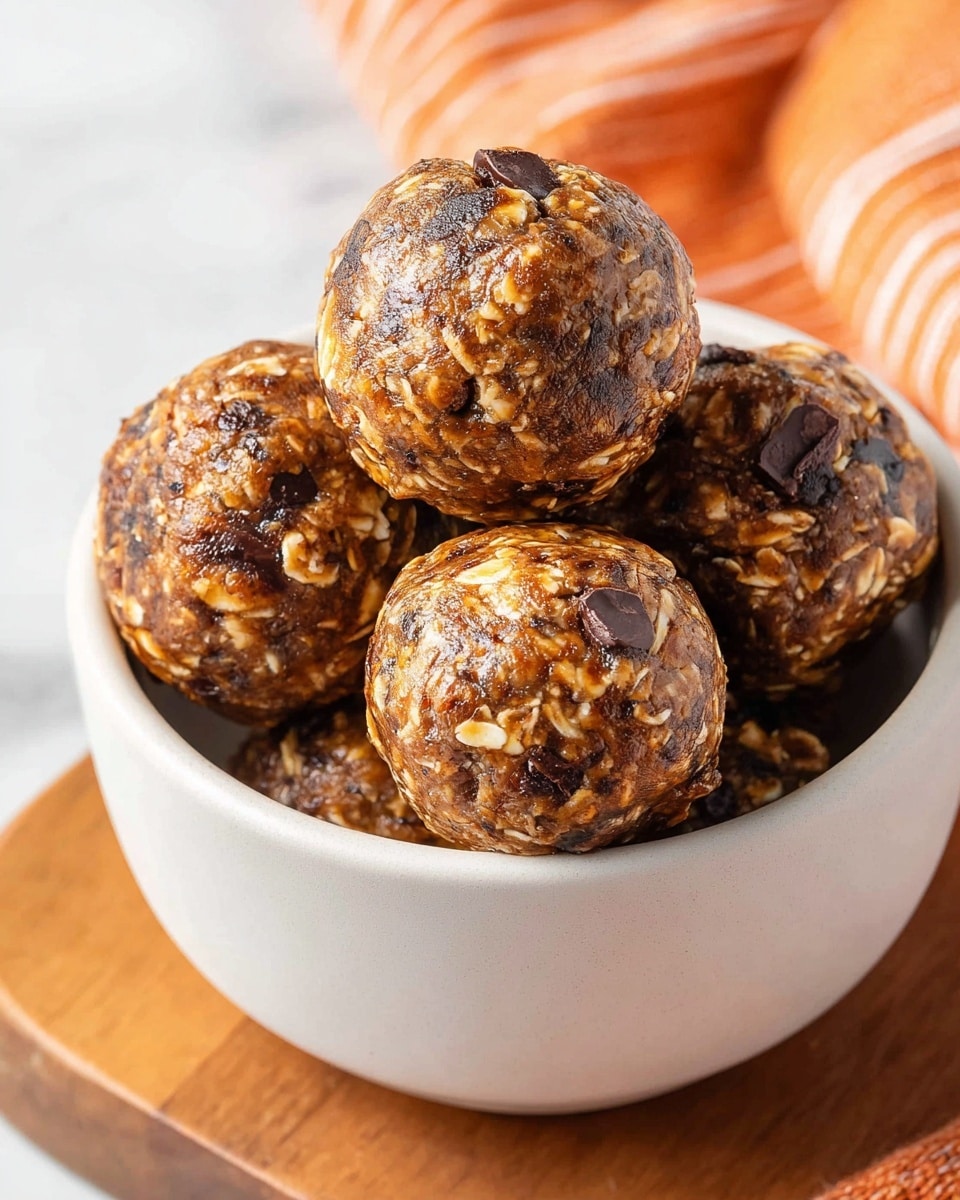 A close-up view of a white bowl filled with six round energy balls. The balls have a textured mix of dark brown and golden tones with visible oats and dark chocolate chunks scattered throughout. The energy balls are tightly packed inside the bowl, stacked in layers with a few on top catching the light to show their sticky, shiny surface. The bowl sits on a wooden cutting board next to an orange-striped cloth, all against a white marbled background. photo taken with an iphone --ar 4:5 --v 7