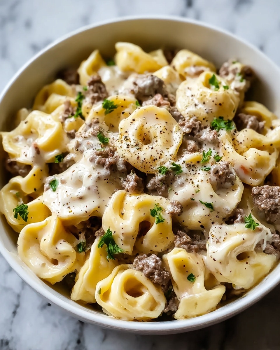 A white bowl filled with tortellini pasta layered with small pieces of browned ground meat scattered throughout. The tortellini are a pale yellow color and have a smooth, soft texture. On top of the pasta and meat is a creamy white sauce that partially covers the layers underneath. The dish is sprinkled with chopped green herbs and freshly ground black pepper, adding specks of green and dark brown on the light surface. The bowl is set on a white marbled texture. photo taken with an iphone --ar 4:5 --v 7