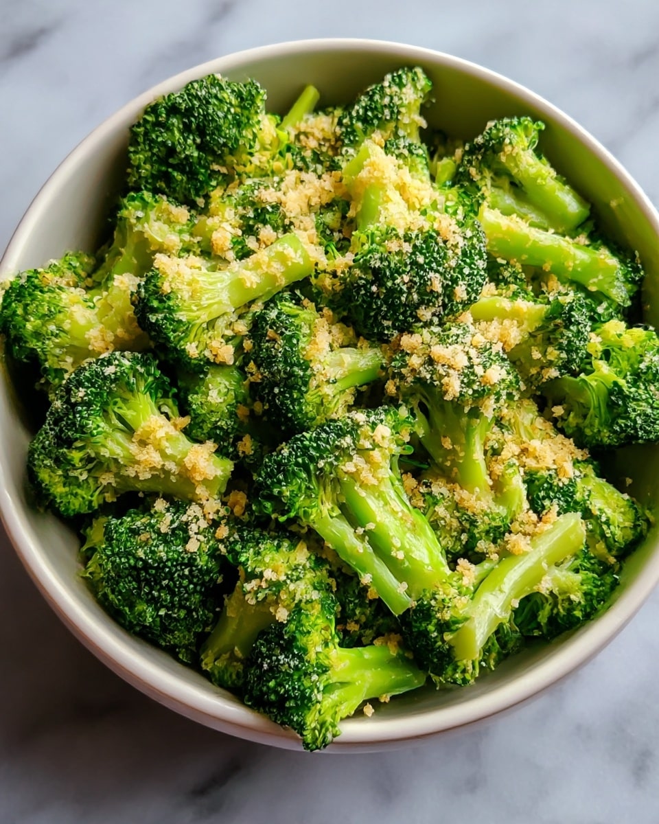A close-up shot of a bowl filled with bright green broccoli florets, each piece coated with small chunks of light yellow garlic and seasoning. The broccoli looks fresh and slightly steamed, giving a soft but firm texture. The bowl is white with a natural brown rim, sitting on a white marbled surface, giving a clean and simple background that makes the green broccoli stand out. photo taken with an iphone --ar 4:5 --v 7